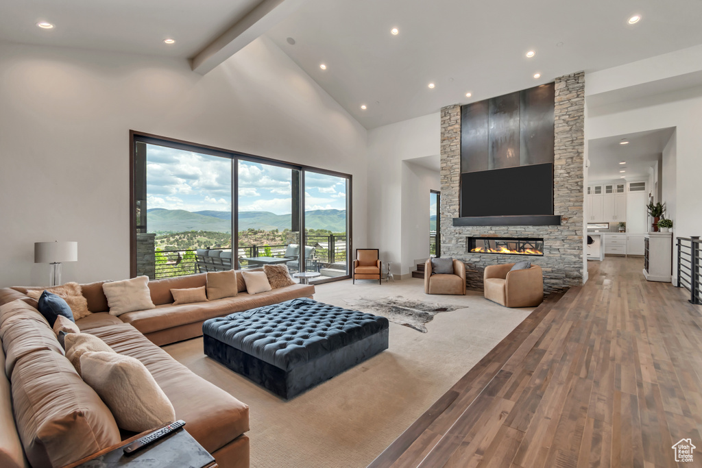 Living area featuring light wood finished floors, high vaulted ceiling, a stone fireplace, recessed lighting, and beam ceiling