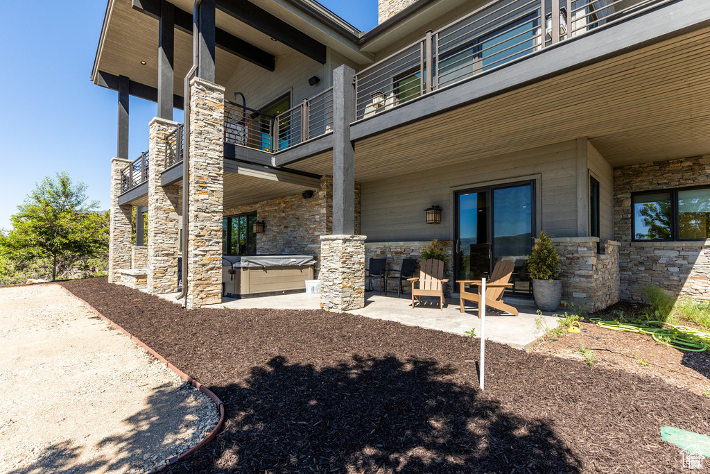 Rear view of property featuring a hot tub, a balcony, stone siding, and a patio area