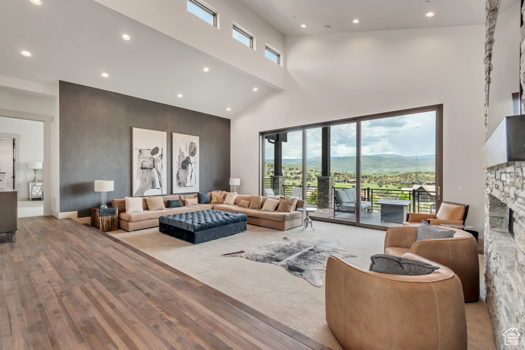 Living area with a towering ceiling, wood finished floors, a stone fireplace, recessed lighting, and a mountain view