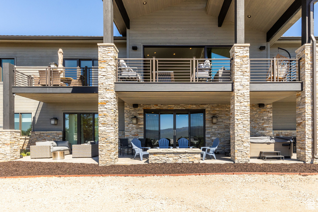 Back of house featuring a balcony, a patio area, a hot tub, and stone siding