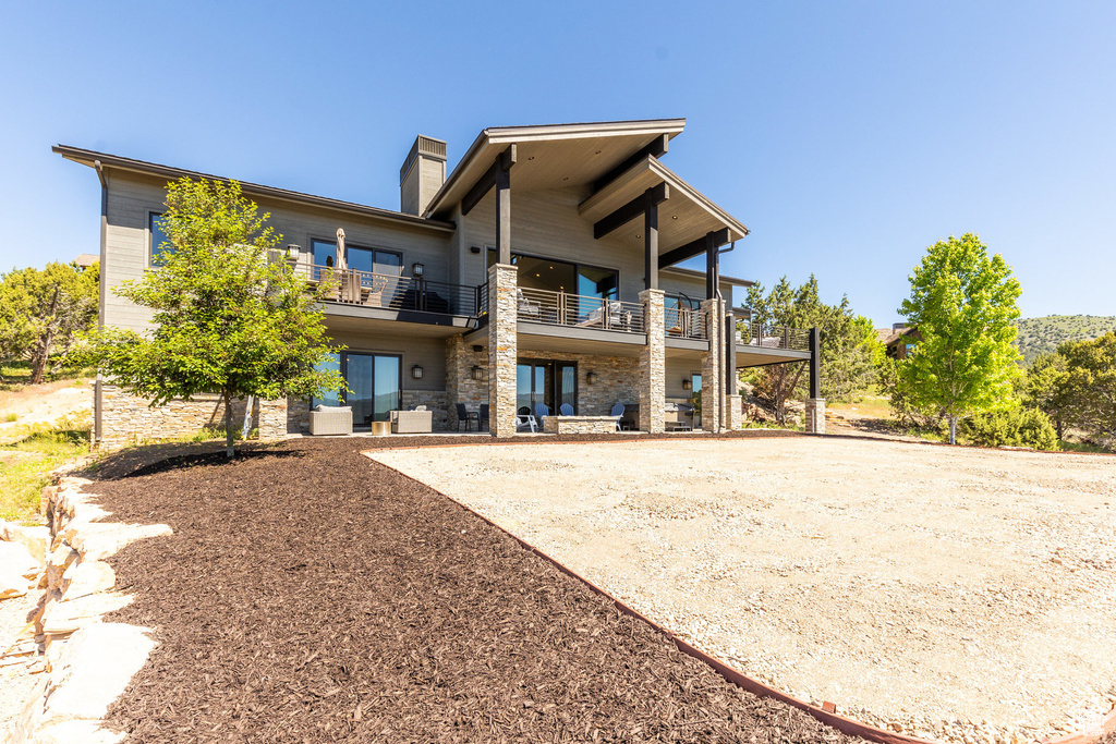 Back of house with a balcony, a chimney, stone siding, and a patio