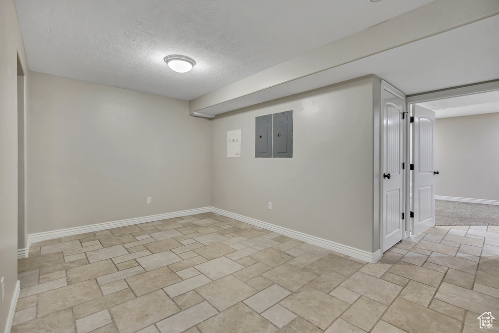 Finished basement with electric panel, a textured ceiling, and baseboards