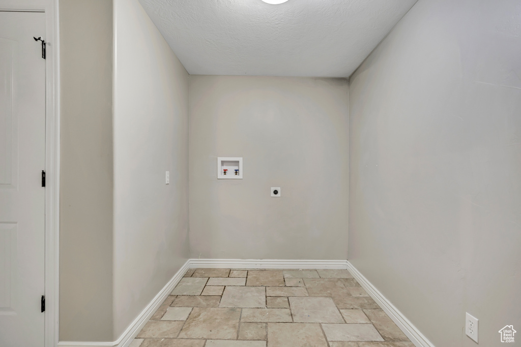 Washroom with hookup for an electric dryer, hookup for a washing machine, stone tile flooring, baseboards, and a textured ceiling