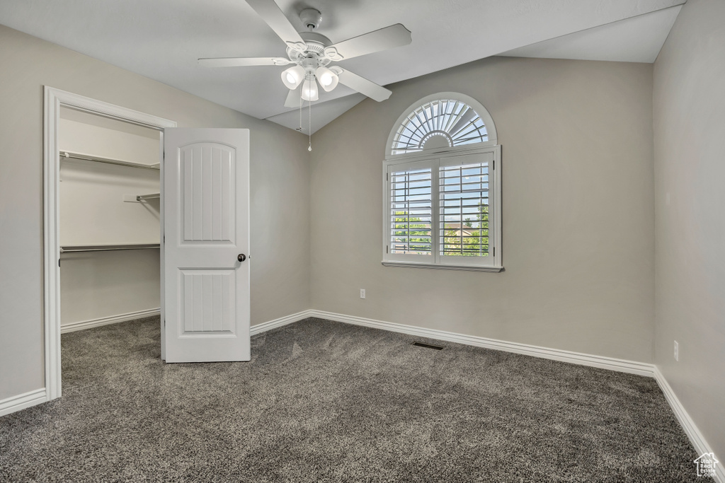 Unfurnished bedroom with carpet, vaulted ceiling, a walk in closet, baseboards, and a ceiling fan