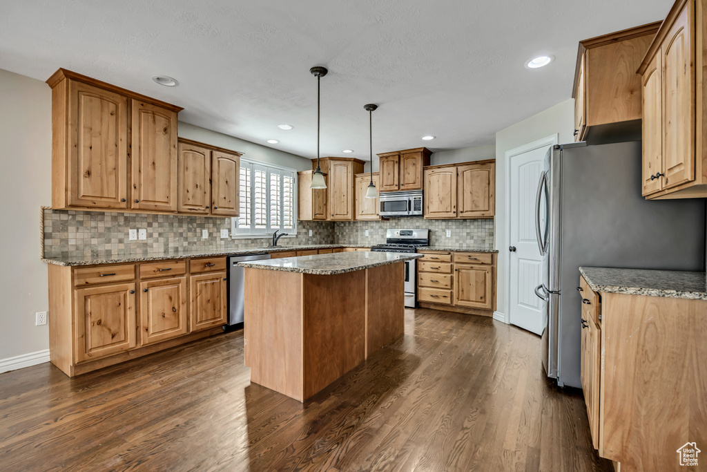 Kitchen with stainless steel appliances, decorative backsplash, dark wood-style flooring, a kitchen island, and light stone countertops