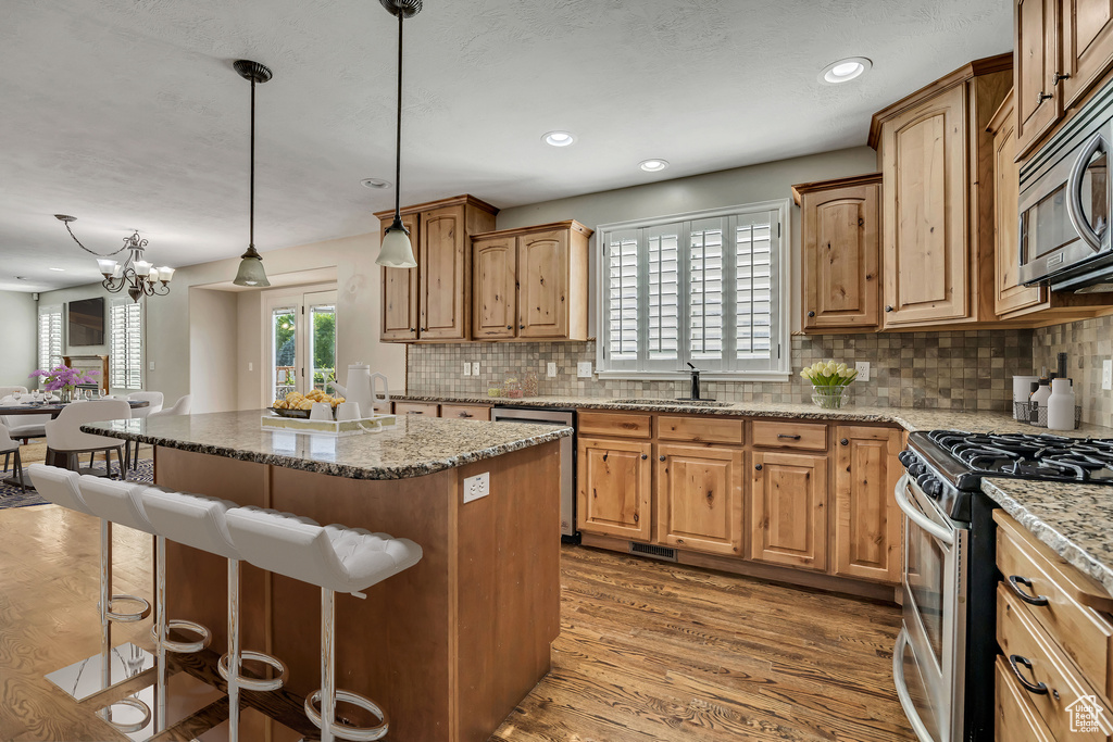 Kitchen featuring appliances with stainless steel finishes, a kitchen breakfast bar, a sink, decorative backsplash, and recessed lighting