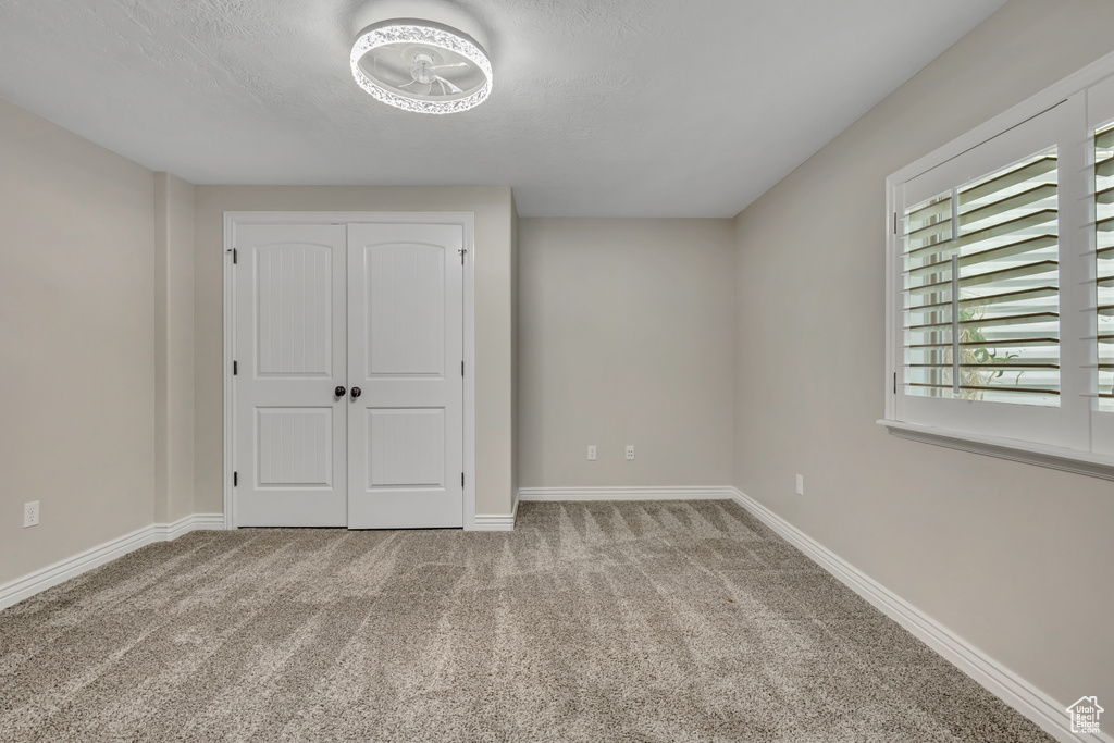 Unfurnished bedroom with carpet flooring, a textured ceiling, baseboards, and a closet