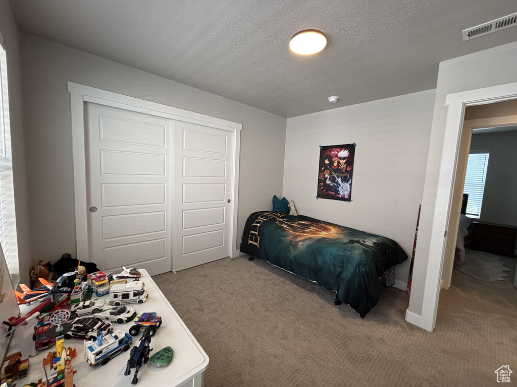 Carpeted bedroom featuring a closet, a textured ceiling, and baseboards