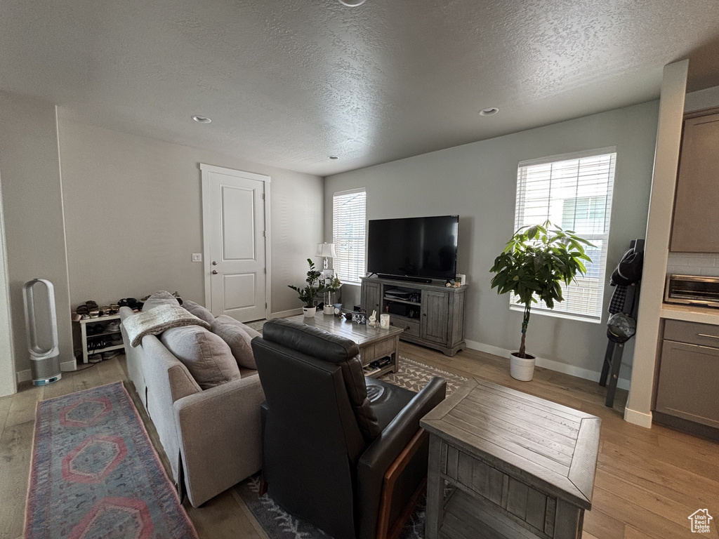 Living room with a textured ceiling, light wood-style flooring, baseboards, and recessed lighting