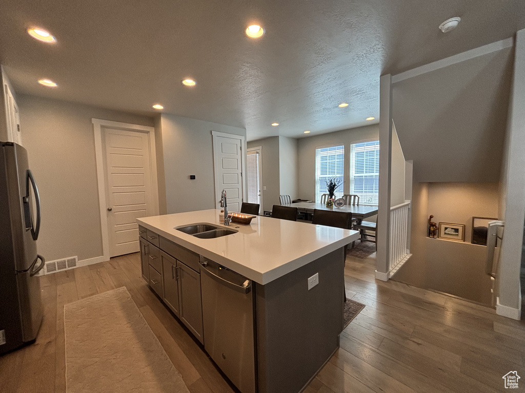 Kitchen featuring a sink, stainless steel appliances, wood finished floors, recessed lighting, and a center island with sink