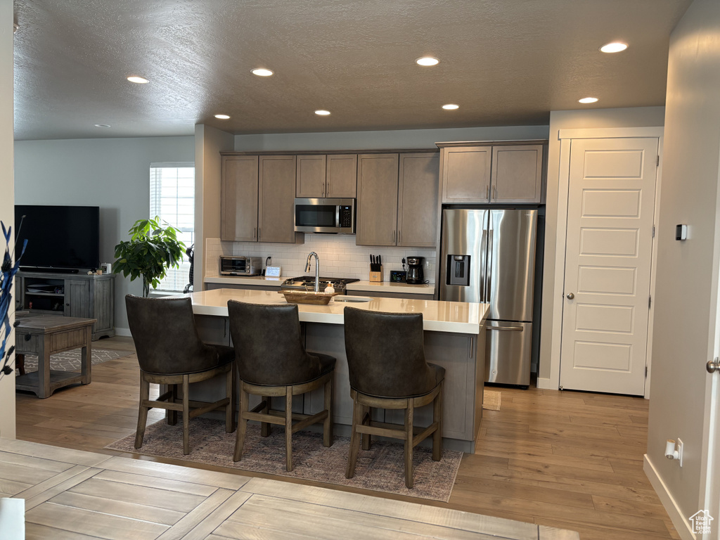 Kitchen featuring stainless steel appliances, light countertops, a center island with sink, tasteful backsplash, and recessed lighting