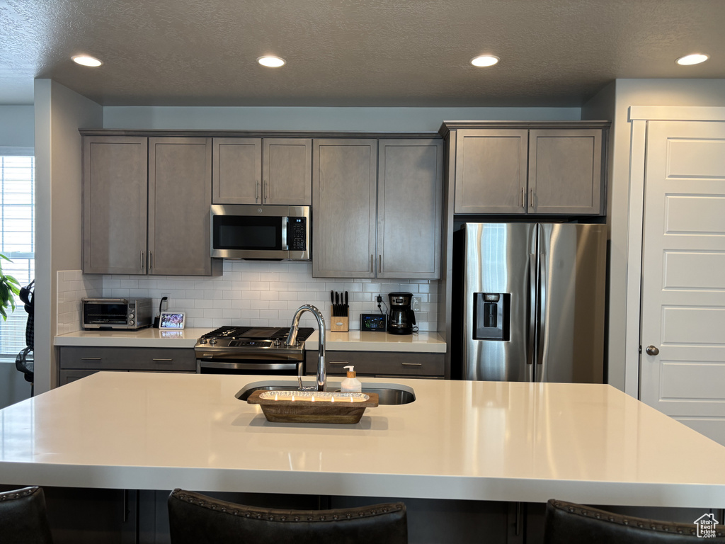 Kitchen featuring appliances with stainless steel finishes, a sink, a breakfast bar, an island with sink, and recessed lighting