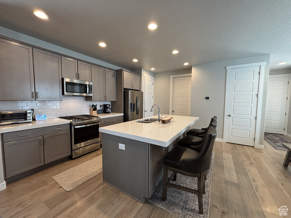 Kitchen featuring appliances with stainless steel finishes, a sink, light wood-style flooring, recessed lighting, and backsplash