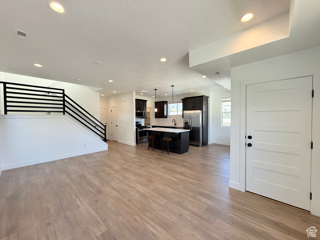 Unfurnished living room featuring light wood-type flooring, stairs, recessed lighting, a sink, and baseboards