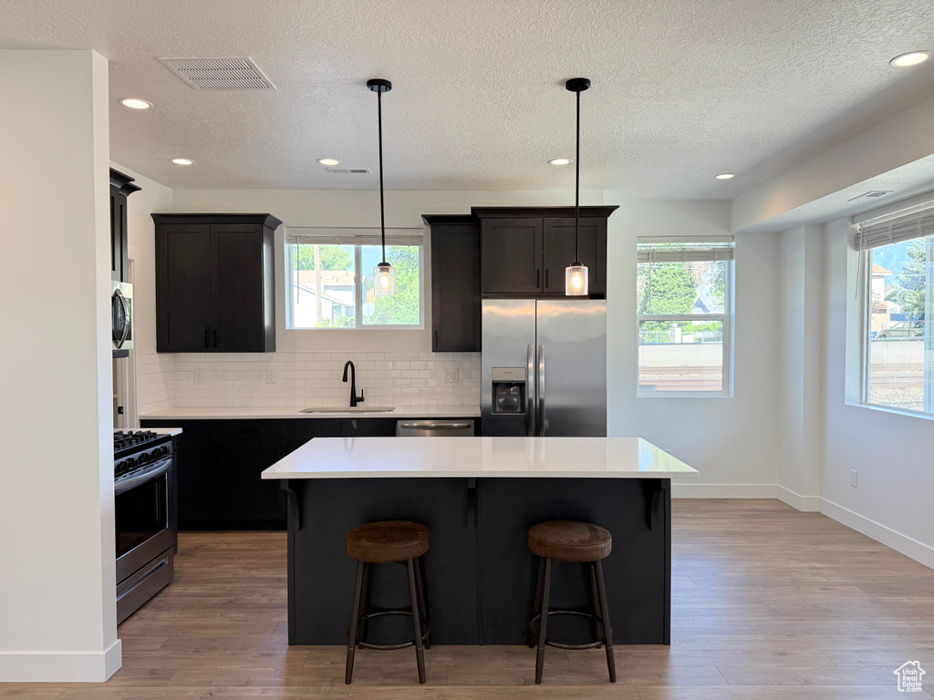 Kitchen with stainless steel appliances, a textured ceiling, a sink, tasteful backsplash, and a kitchen breakfast bar