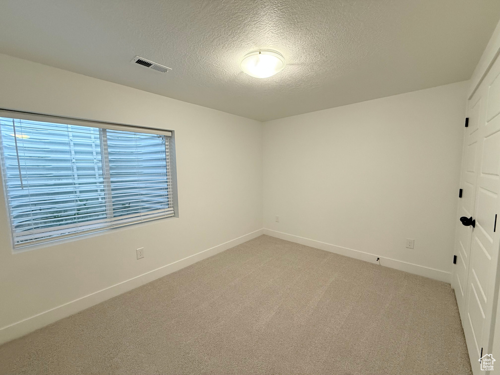Empty room with a textured ceiling, baseboards, and light carpet