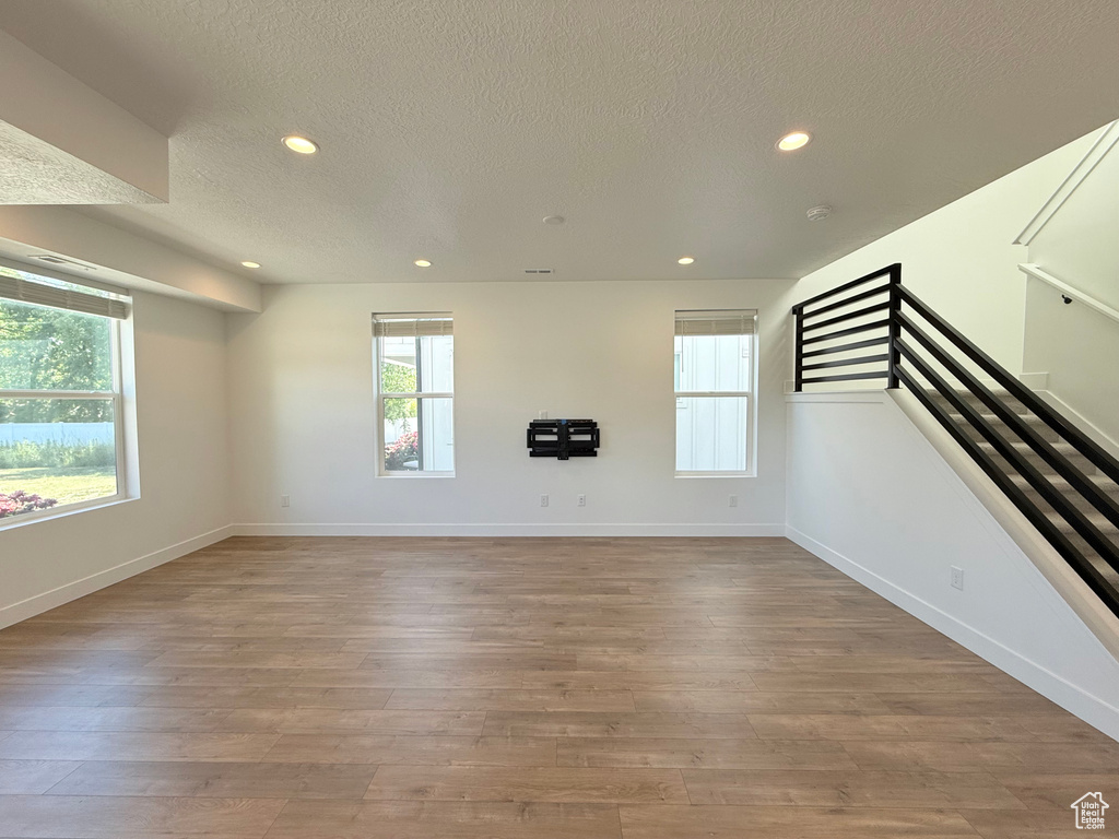 Unfurnished living room featuring a textured ceiling, recessed lighting, healthy amount of natural light, baseboards, and light wood-type flooring