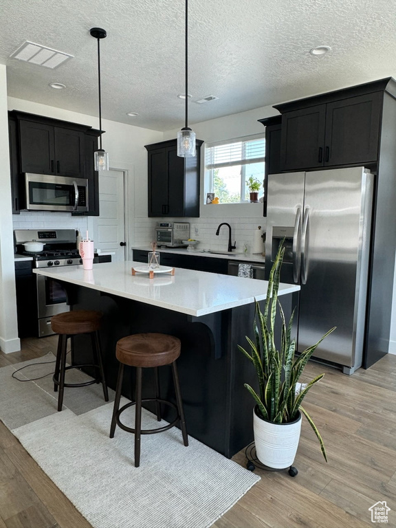 Kitchen with appliances with stainless steel finishes, dark cabinetry, decorative backsplash, light wood finished floors, and a textured ceiling