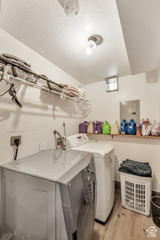 Laundry room featuring independent washer and dryer, electric panel, light wood-style floors, and a textured ceiling