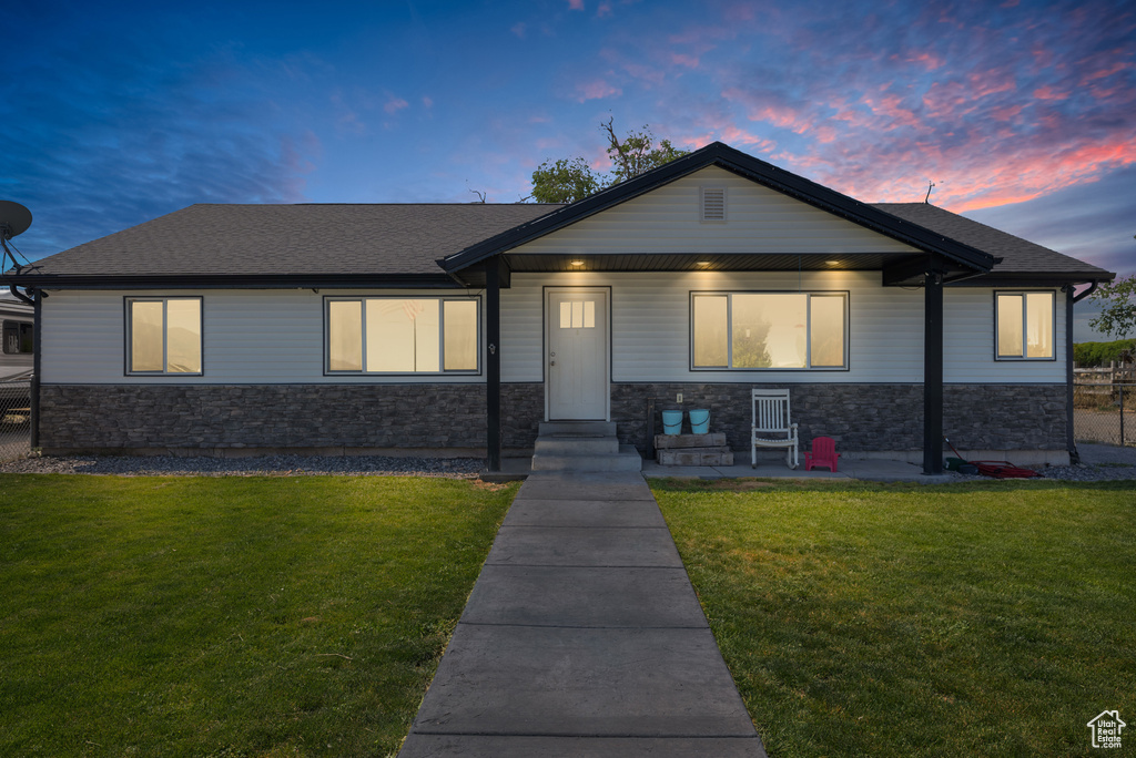 View of front of home featuring stone siding, a front yard, and a shingled roof