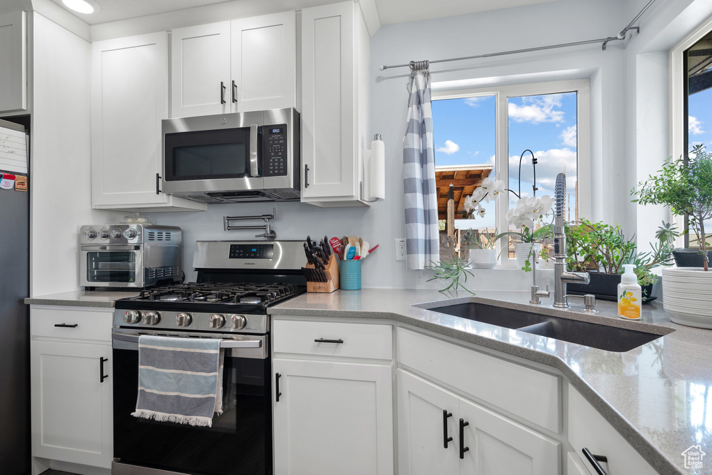 Kitchen with appliances with stainless steel finishes, a sink, white cabinets, and light stone counters
