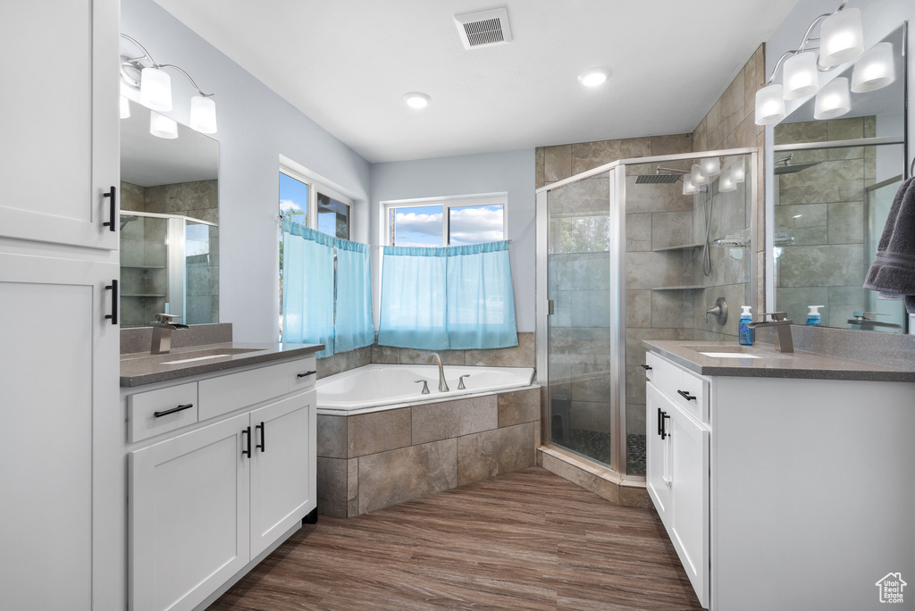 Bathroom with two vanities, a shower stall, a garden tub, wood finished floors, and recessed lighting