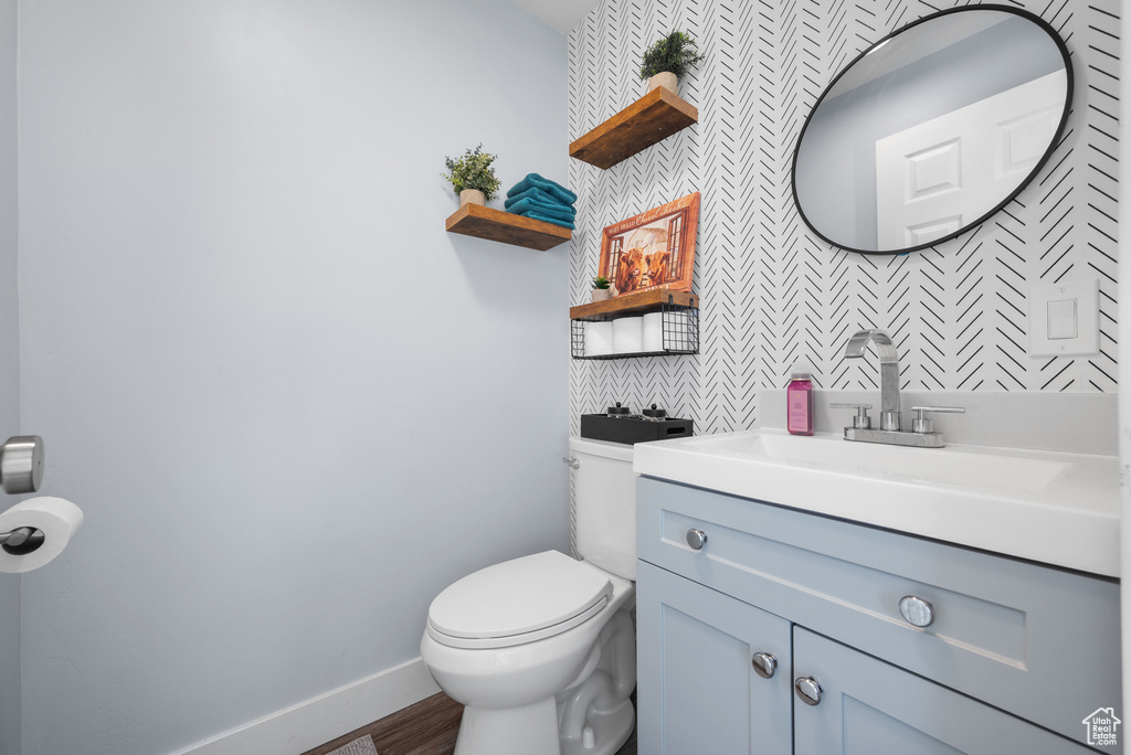Half bathroom featuring toilet, vanity, baseboards, tasteful backsplash, and wood finished floors