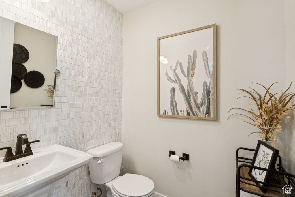 Half bathroom featuring toilet, a sink, tile walls, and tasteful backsplash
