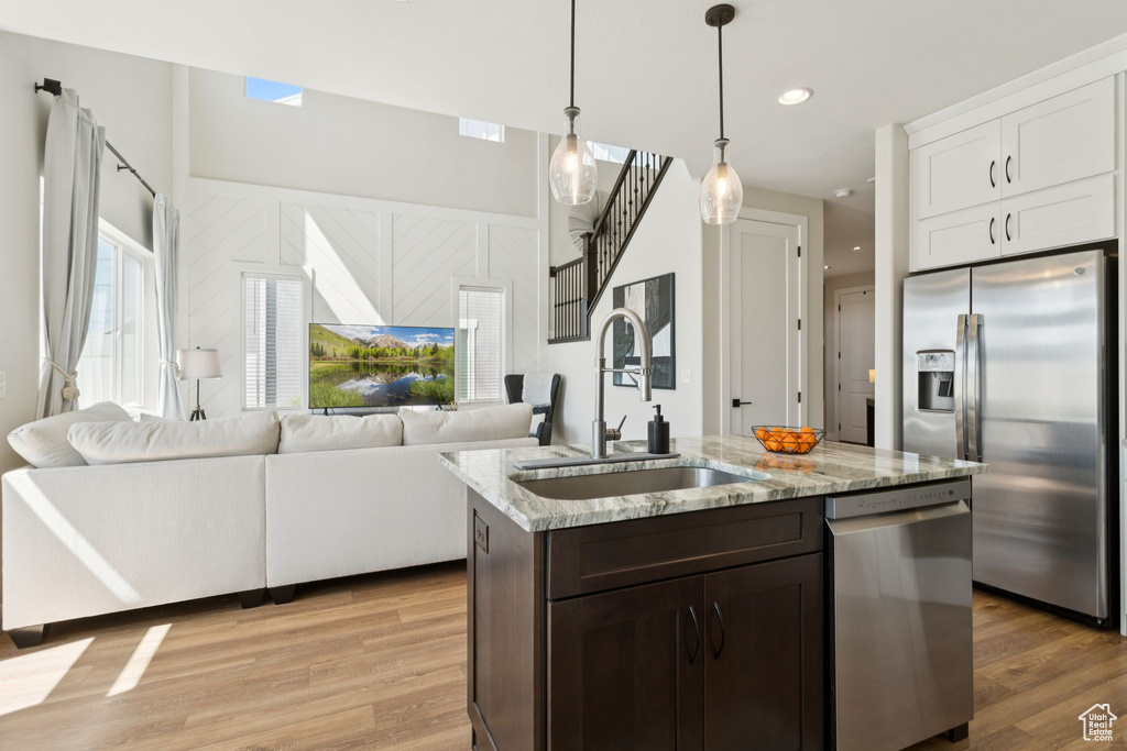 Kitchen featuring appliances with stainless steel finishes, a sink, light wood-style floors, hanging light fixtures, and dark brown cabinetry