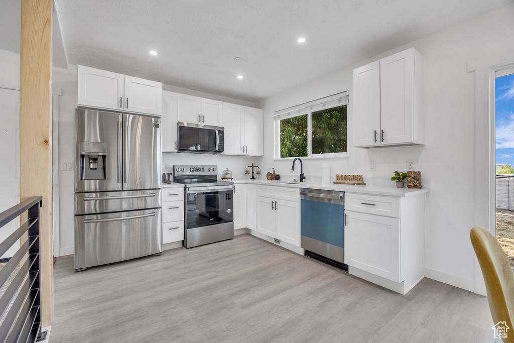 Kitchen featuring stainless steel appliances, light wood-style floors, white cabinetry, a sink, and light countertops