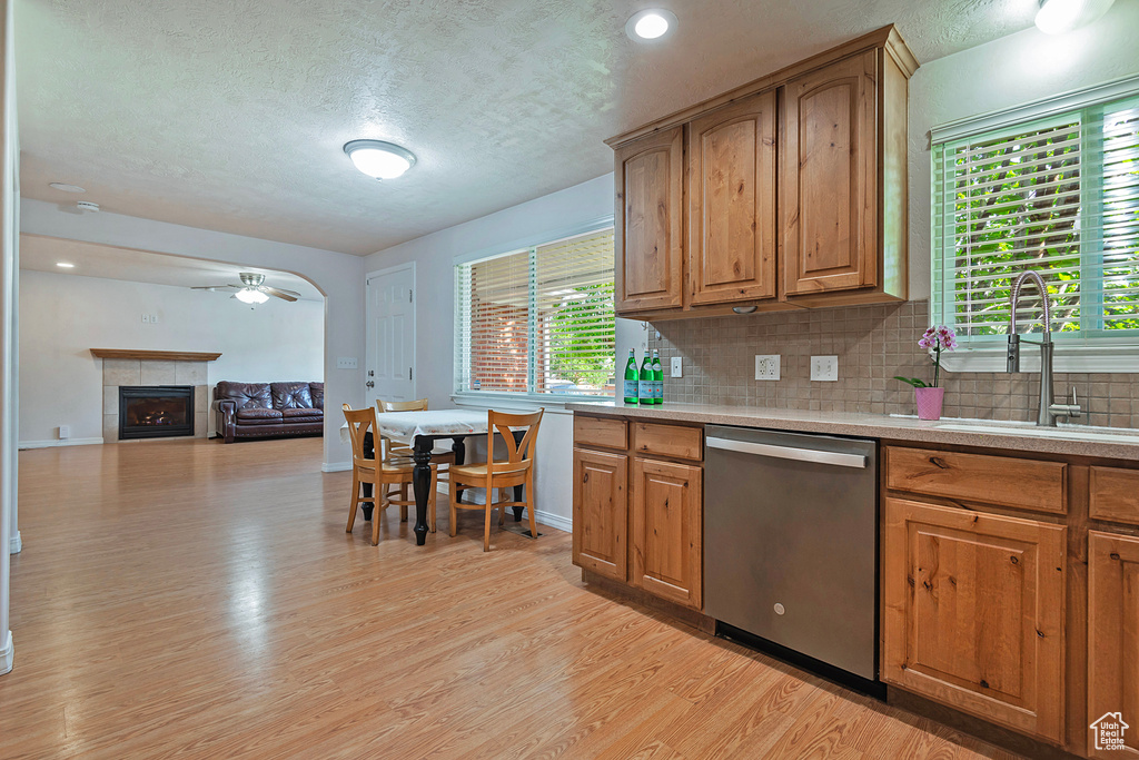 Kitchen featuring stainless steel dishwasher, a sink, a textured ceiling, light wood-style floors, and backsplash
