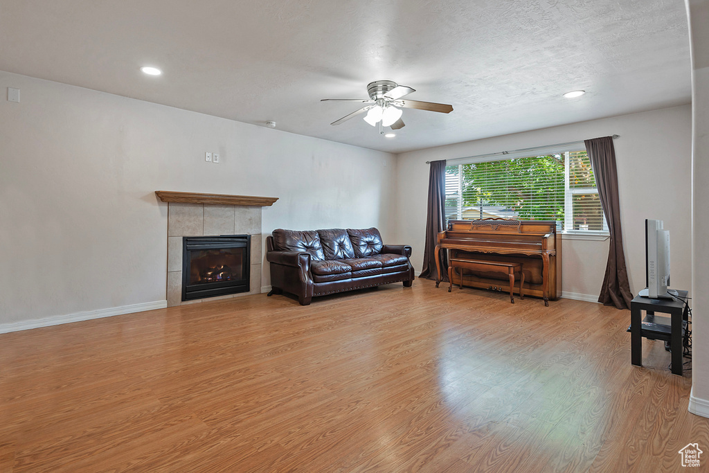 Living room featuring a ceiling fan, light wood finished floors, baseboards, recessed lighting, and a tile fireplace