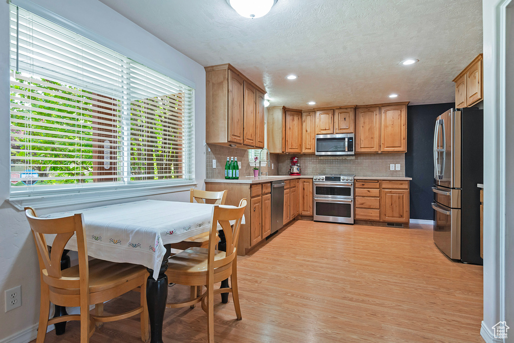 Kitchen featuring stainless steel appliances, light countertops, backsplash, light wood-style flooring, and recessed lighting