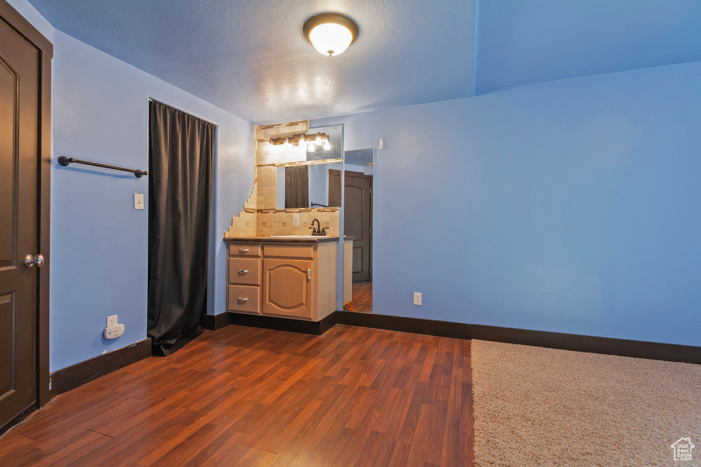 Bathroom with wood finished floors, baseboards, vanity, decorative backsplash, and a textured ceiling