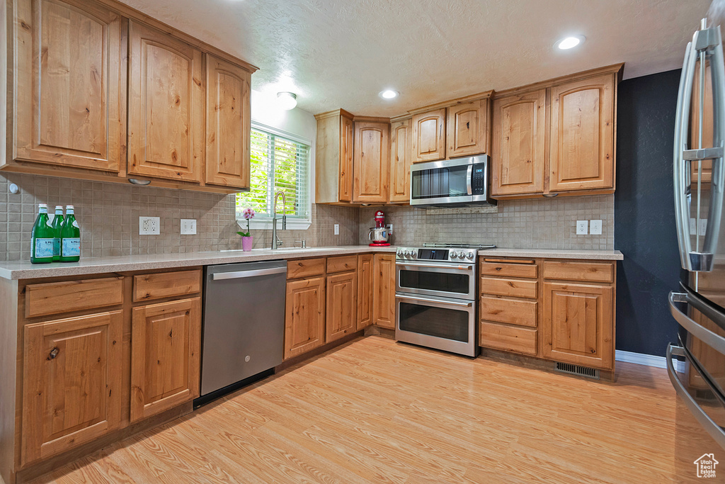 Kitchen with stainless steel appliances, light wood finished floors, light countertops, tasteful backsplash, and recessed lighting