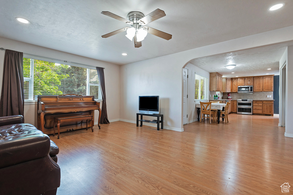 Living area with light wood-style floors, arched walkways, recessed lighting, ceiling fan, and plenty of natural light