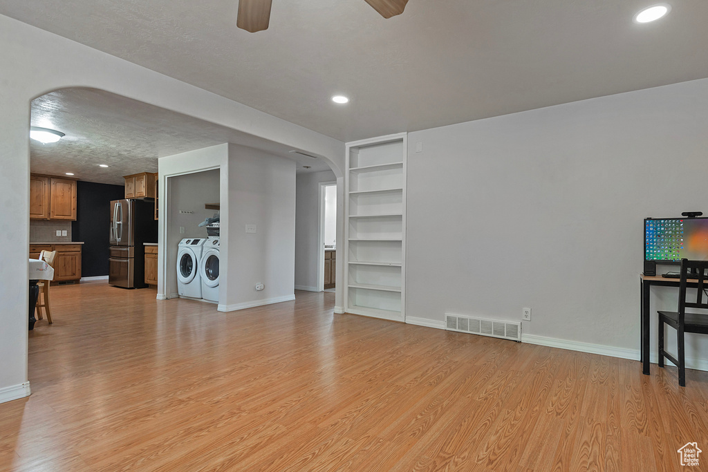 Unfurnished living room with separate washer and dryer, arched walkways, a ceiling fan, built in shelves, and light wood-style flooring