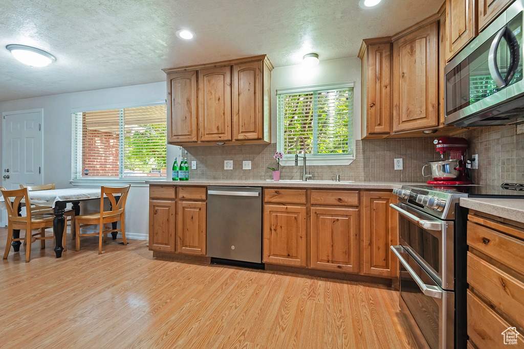 Kitchen featuring appliances with stainless steel finishes, light wood-style floors, light countertops, backsplash, and a textured ceiling
