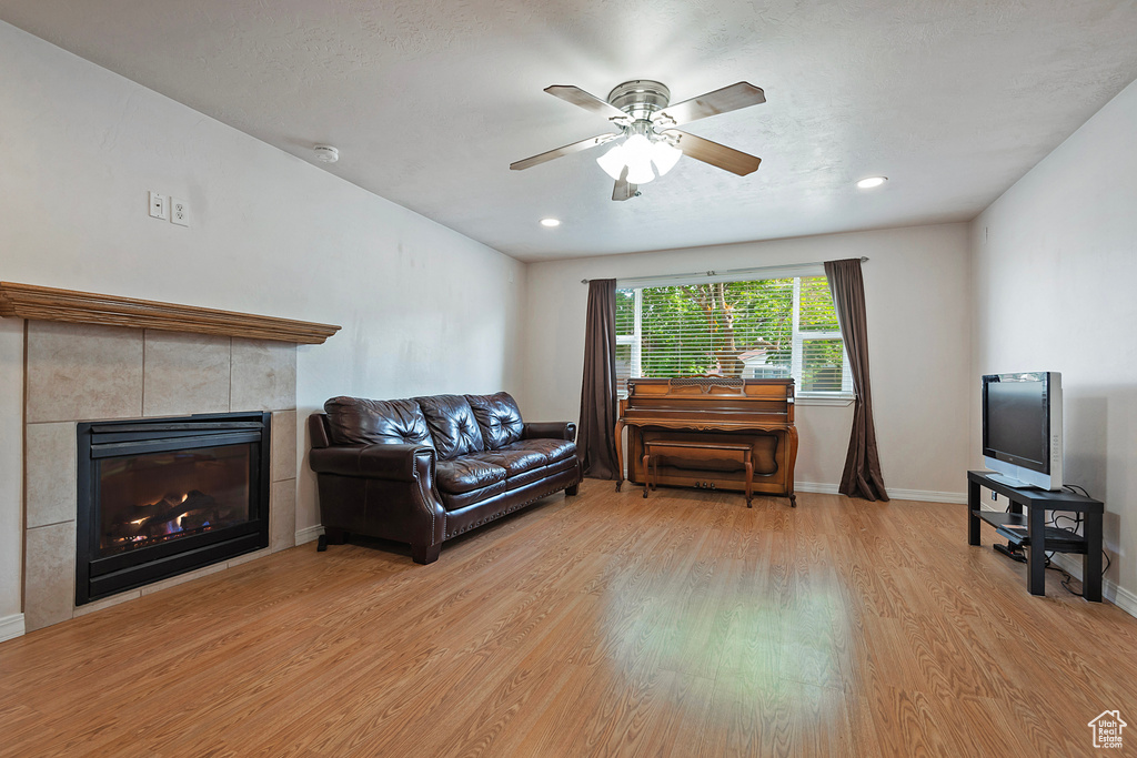 Living area with light wood finished floors, a ceiling fan, a tile fireplace, baseboards, and recessed lighting