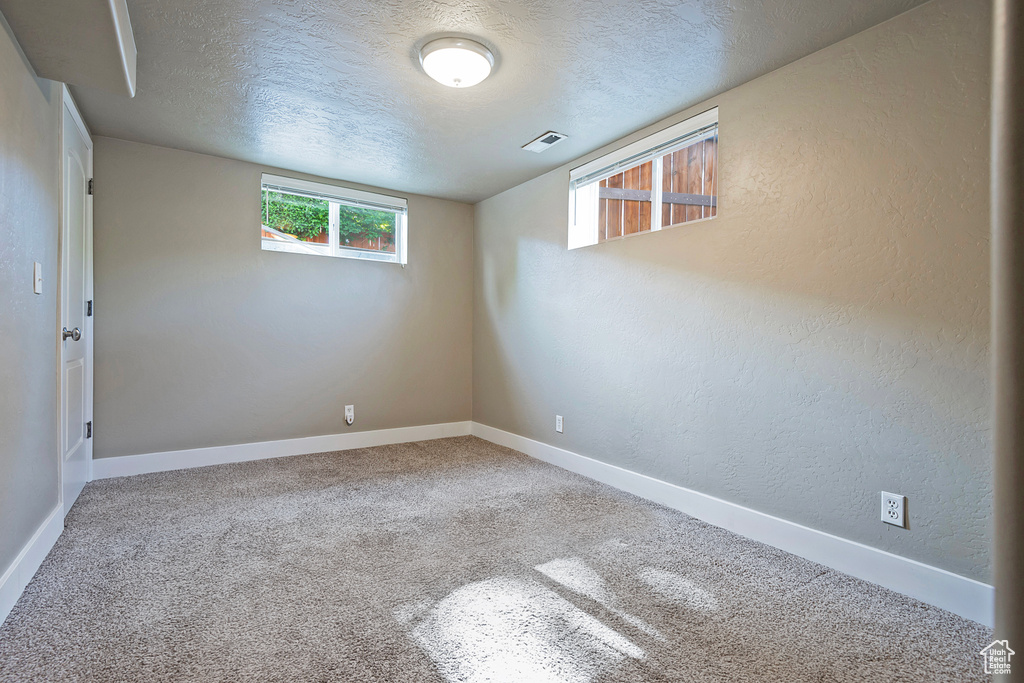 Carpeted empty room with a textured ceiling, baseboards, and a textured wall