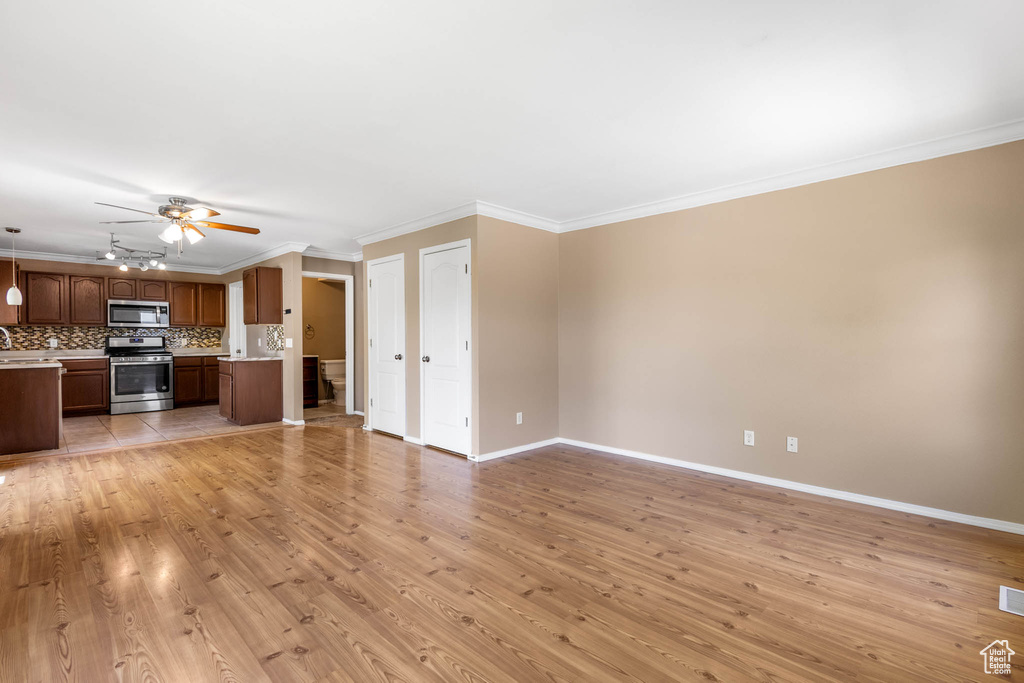 Unfurnished living room with ceiling fan, light wood-style floors, crown molding, and baseboards