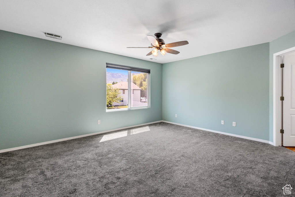 Carpeted spare room featuring ceiling fan and baseboards