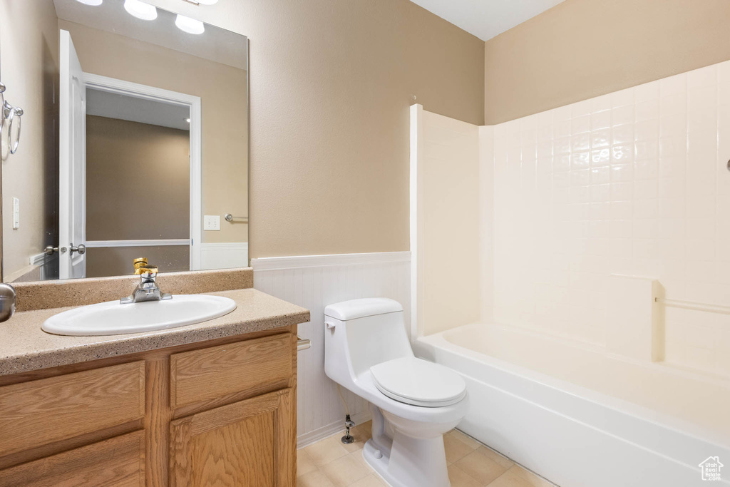 Full bath with a wainscoted wall, toilet, vanity, tile patterned floors, and shower / tub combination