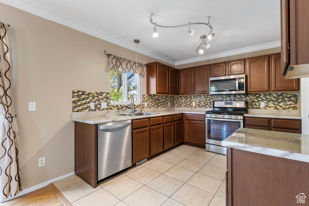 Kitchen with stainless steel appliances, a sink, light countertops, ornamental molding, and decorative backsplash