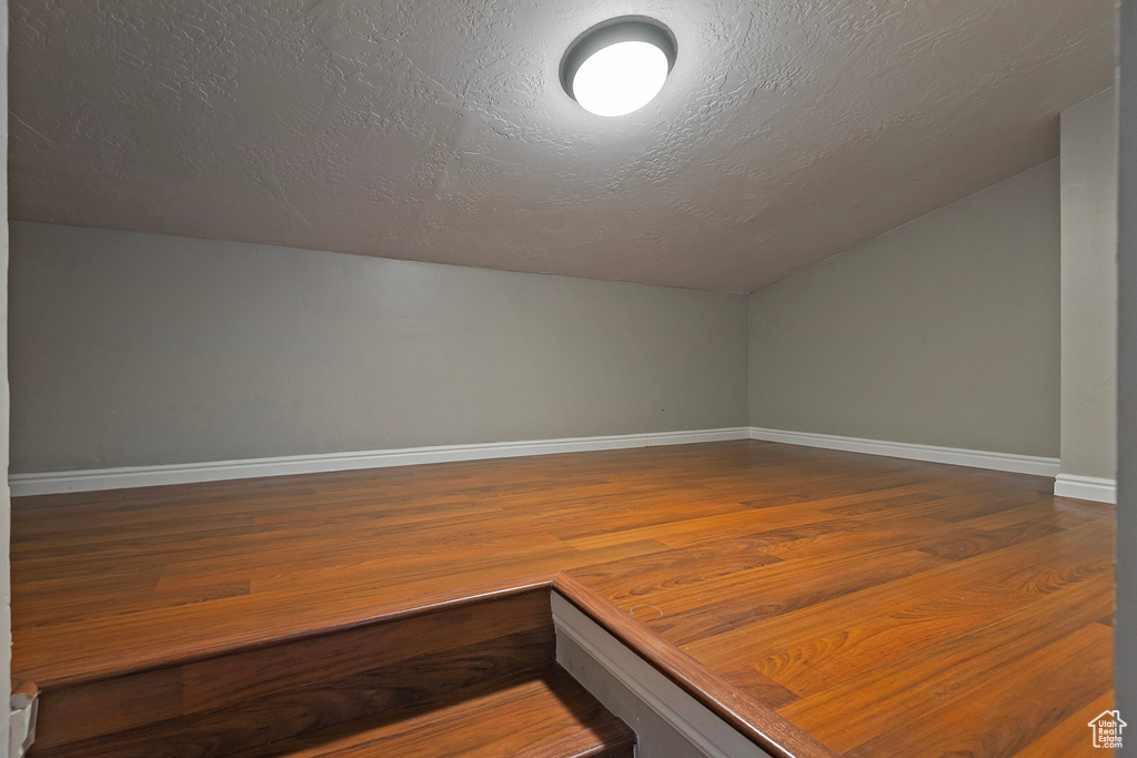 Additional living space featuring vaulted ceiling, wood finished floors, baseboards, and a textured ceiling