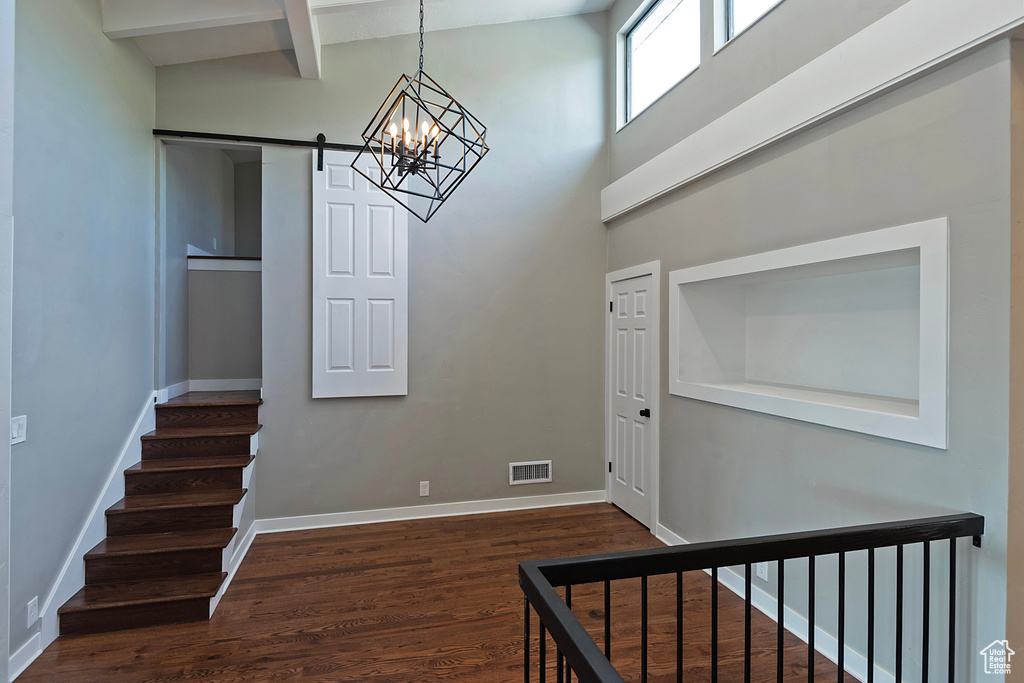 Stairway featuring a barn door, wood finished floors, a chandelier, baseboards, and beamed ceiling