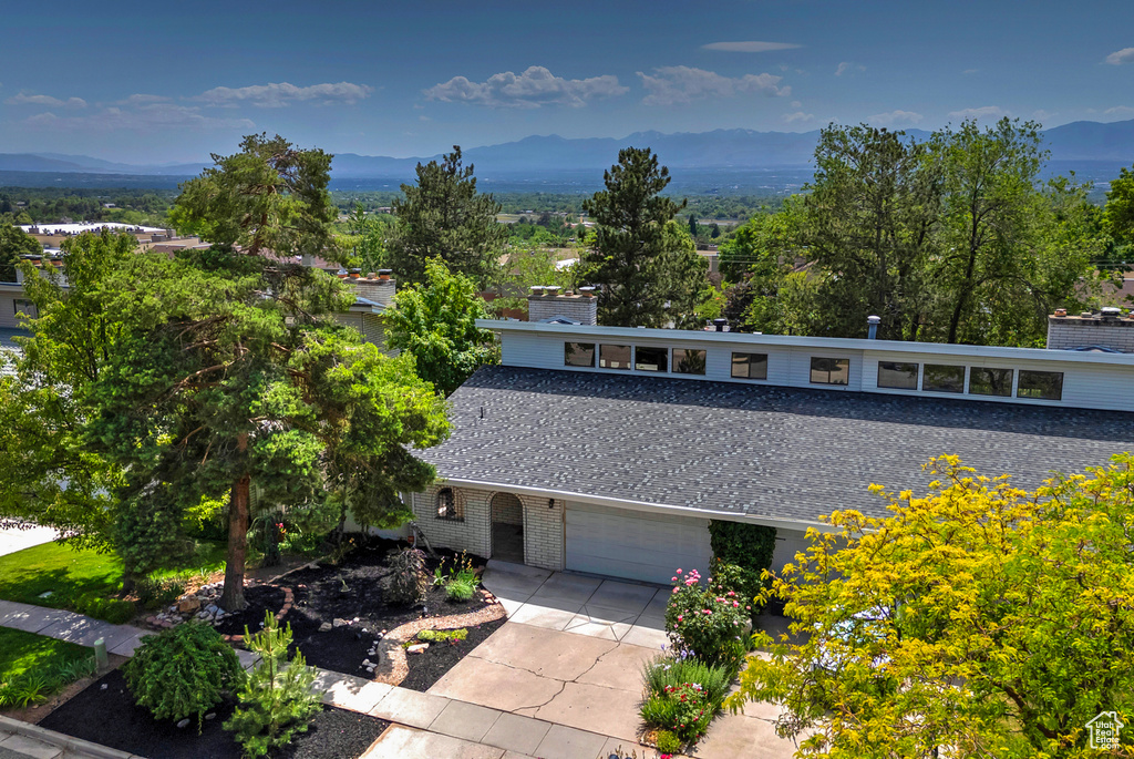 View of front facade with a mountain view, a garage, concrete driveway, brick siding, and a chimney