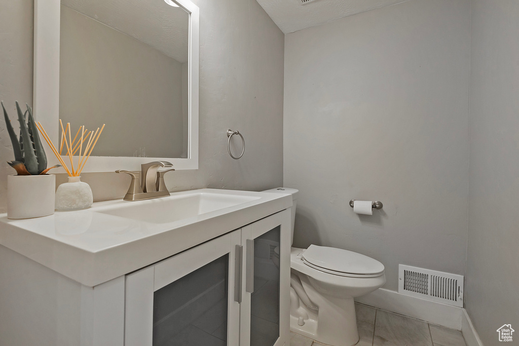 Half bathroom with toilet, vanity, baseboards, and tile patterned flooring