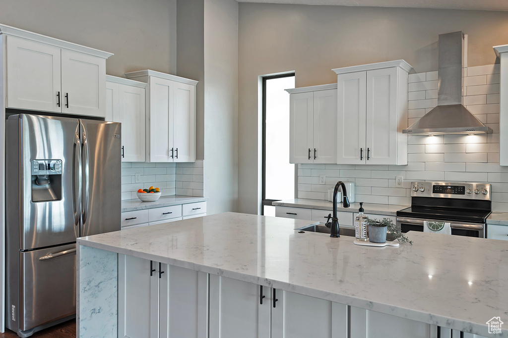 Kitchen with stainless steel appliances, wall chimney exhaust hood, white cabinets, backsplash, and lofted ceiling