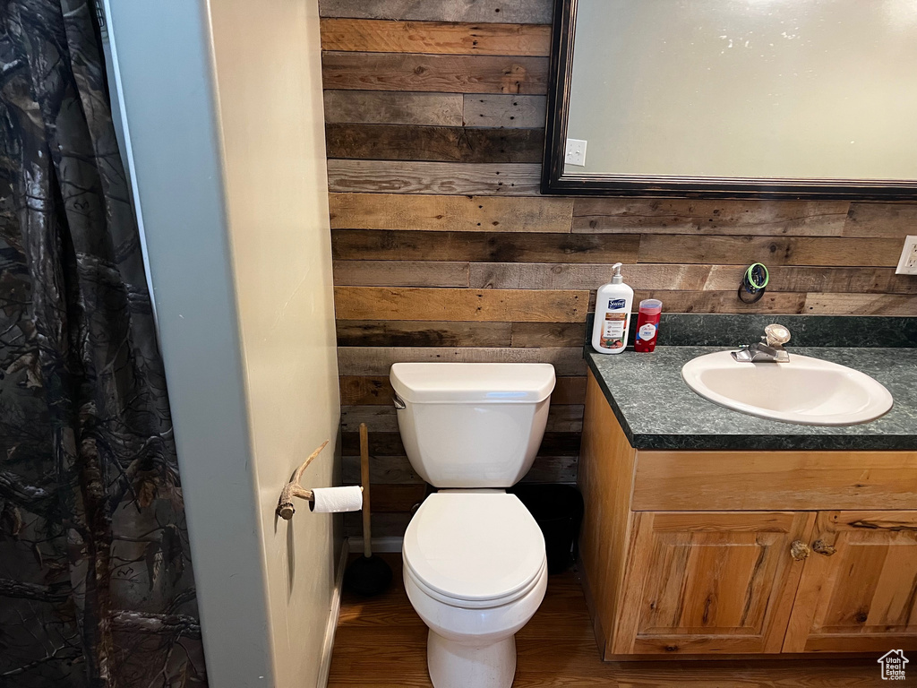 Full bath with toilet, wood walls, vanity, and wood finished floors